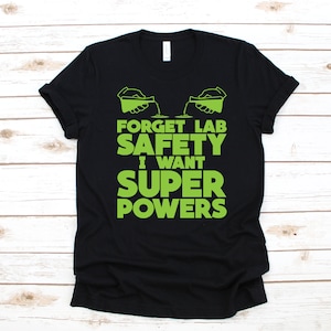 May include: Black t-shirt with green text that reads "Forget Lab Safety I Want Super Powers". Two green cartoon hands are pouring liquid from beakers.