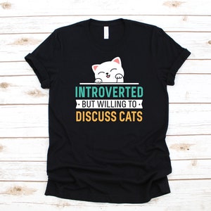 May include: Black t-shirt featuring a white cat illustration and the text "Introverted, but willing to discuss cats".