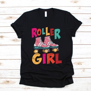 Może przedstawiać: Czarny t-shirt z kolorowym nadrukiem graficznym. Projekt przedstawia słowa "ROLLER GIRL" w stylu retro, z parą różowych rolek pośrodku. Koszulka wykonana jest z miękkiego materiału i ma klasyczny okrągły dekolt.