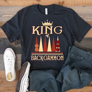 May include: A black t-shirt with a graphic design of a backgammon board and the text "King of Backgammon". The graphic features a crown, red and orange game pieces, and a beige backgammon board.