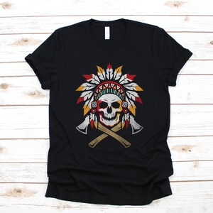 May include: Black t-shirt with a graphic of a skull wearing a Native American headdress with red, yellow, blue, and white feathers. Two crossed tomahawks are behind the skull.