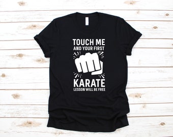 May include: Black t-shirt with white text that reads "Touch me and your first karate lesson will be free". A white fist graphic is above the text.