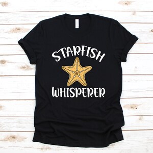 May include: Black t-shirt with white text that reads "Starfish Whisperer" and a yellow starfish graphic.