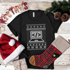 May include: Black t-shirt with a white Christmas sweater design featuring a laptop with code symbols. The design includes snowflakes and Christmas trees.