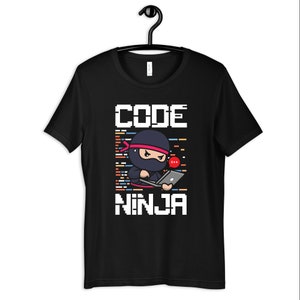 Puede incluir: Camiseta negra con un gráfico blanco de un ninja de dibujos animados codificando en una computadora portátil. El texto "CODE NINJA" está impreso en blanco debajo de la imagen. El ninja tiene un globo de diálogo rojo con el texto "C++" en él.