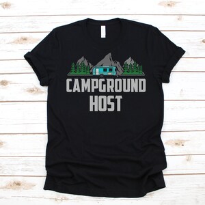 May include: Black t-shirt featuring a graphic of a camper van in a mountain landscape. The text "Campground Host" is printed in grey below the image.