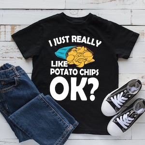 Puede incluir: Camiseta negra con texto blanco que dice "Me gustan mucho las patatas fritas ¿OK?" y una imagen de dibujos animados de una bolsa de patatas fritas.