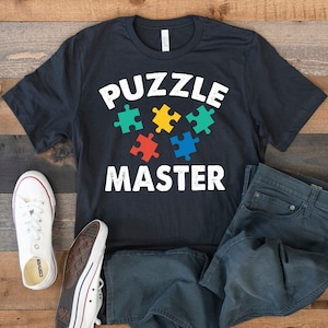 May include: A black t-shirt with the text "PUZZLE MASTER" in white with a graphic of five colorful puzzle pieces.