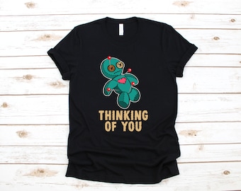 May include: Black t-shirt with a green voodoo doll graphic and the text "Thinking of You" in gold lettering.