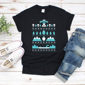 Könnte beinhalten: Schwarzes T-Shirt mit einem blauen und weißen Weihnachtspullover-Design mit Außerirdischen, einem Bigfoot und einem Seeungeheuer.