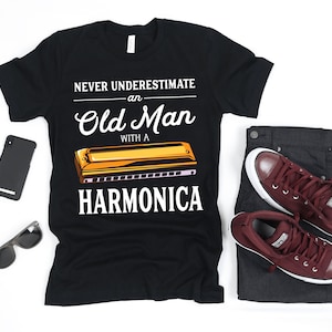 May include: Black t-shirt with the text "Never underestimate an Old Man with a Harmonica" and a graphic of a harmonica.
