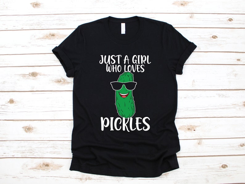 以下が含まれることがあります： 黒いTシャツに、サングラスをかけたピクルスの白いグラフィックと「Just a girl who loves pickles」というテキストがプリントされています。