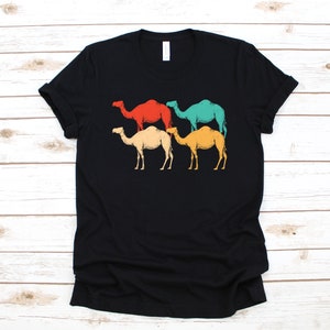 Puede incluir: Camiseta negra con un gráfico de estilo retro de cuatro camellos en diferentes colores: rojo, verde azulado, amarillo y crema.