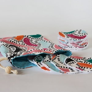 Peut inclure: Un ensemble de disques démaquillants réutilisables dans un sac à cordon. Les disques sont en coton blanc avec un imprimé abstrait coloré. Le sac est en tissu turquoise avec un imprimé abstrait blanc et noir.