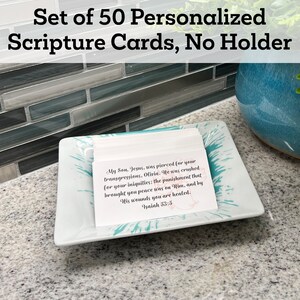 May include: A set of 50 personalised scripture cards in a white dish with a turquoise design. The cards are white with black text and a scripture quote from Isaiah 53:5. The text reads: "My Son, Jesus, was pierced for your transgressions, Olivia. He was crushed for your iniquities: the punishment that brought you peace was on Him, and by His wounds you are healed. Isaiah 53:5"