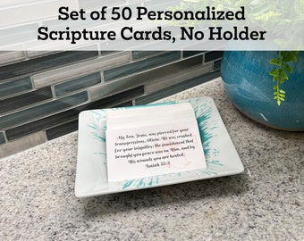 Op de afbeelding: Een set van 50 gepersonaliseerde schriftkaarten in een wit schaaltje met een turquoise design. De kaarten zijn wit met zwarte tekst en een bijbelcitaat uit Jesaja 53:5. De tekst luidt: "Mijn Zoon, Jezus, werd doorboord voor uw overtredingen, Olivia. Hij werd verbrijzeld voor uw ongerechtigheden: de straf die u vrede bracht, was op Hem, en door Zijn wonden bent u genezen. Jesaja 53:5"