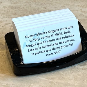 May include: A stack of white cards with a black holder. The cards feature a blue floral design and text in Spanish that reads: "No prevalecer&aacute; ninguna arma que se forje contra ti, Nikki. Toda lengua que te acuse ser&aacute; refutada. Esta es la herencia de mis siervos, la justicia que de m&iacute; procede! Isa&iacute;as 54:17"