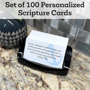 May include: A set of 100 white scripture cards with a blue anchor design. The cards are in a black card holder on a granite countertop. The text on the card reads: "Lucas, I prepare a table before you in the presence of your enemies. I honor you by anointing your head with oil; your cup overflows. Psalm 23:5"