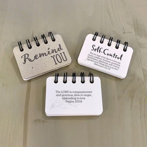 May include: Three small, white, spiral bound notebooks with inspirational quotes and bible verses. The first notebook says "Remind You". The second notebook says "Self-Control" and includes a bible verse from Galatians 5:22-23. The third notebook says "The LORD is compassionate and gracious, slow to anger, abounding in love. Psalm 103:8".