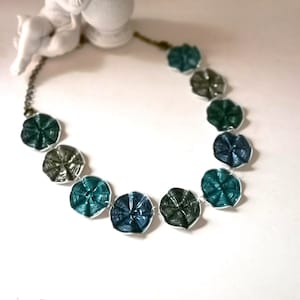 Könnte beinhalten: Eine Halskette aus recycelten Aluminium-Dosenlaschen. Die Laschen sind zu Blumen geformt und in einem Farbverlauf von Blau und Grün angeordnet.
