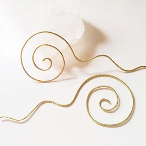 Könnte beinhalten: Ein Paar goldfarbene Ohrringe mit einem Spiraldesign. Die Ohrringe sind aus dünnem Draht gefertigt und haben einen zarten, verspielten Look.