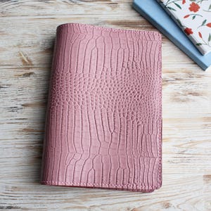 May include: A pink leather-bound notebook with a crocodile-embossed pattern.