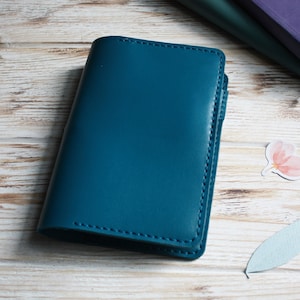May include: A solid teal notebook cover with visible stitching along the edges and a small pen loop on the right side. The cover has a smooth, matte finish and a rectangular shape with rounded corners, presenting a clean and functional design.