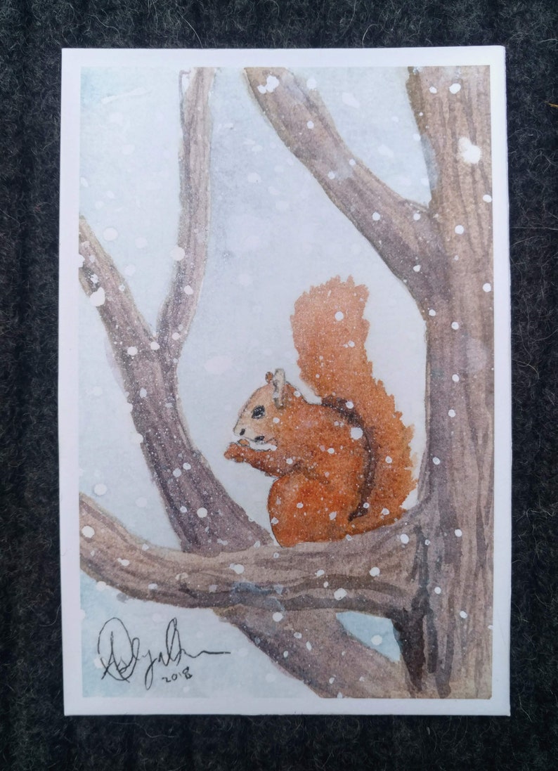 Puede incluir: Una pintura de acuarela de una ardilla roja sentada en una rama de un &aacute;rbol en un bosque nevado. La ardilla mira hacia la izquierda y tiene la cola enroscada alrededor de su cuerpo. El fondo es de color azul claro con puntos blancos que representan la nieve.