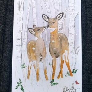 Puede incluir: Pintura acuarela de dos ciervos en un bosque nevado. Los ciervos son marrones con manchas blancas y est&aacute;n de pie uno cerca del otro. El fondo es azul claro con &aacute;rboles blancos y nieve.