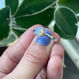May include: A silver ring with a white opal gemstone. The ring is on a finger with blue nail polish.
