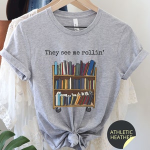 May include: Grey t-shirt with the text "They see me rollin'" and a graphic of a rolling bookshelf filled with books.