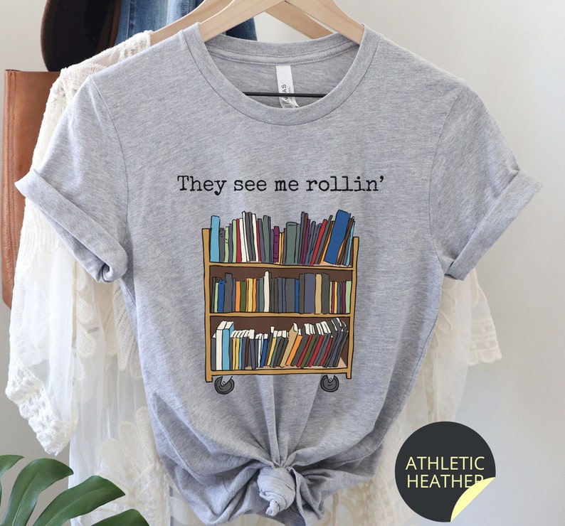 May include: Grey t-shirt with the text "They see me rollin'" and a graphic of a rolling bookshelf filled with books.