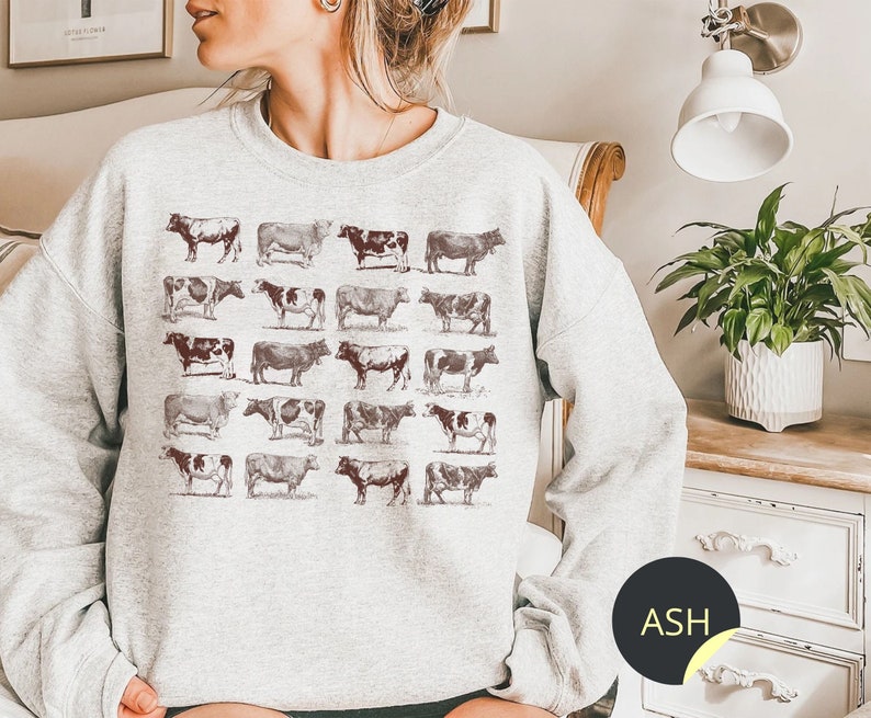 May include: A gray sweatshirt with a vintage-style print of cows in various poses. The print is in shades of brown and black, and the sweatshirt has a relaxed fit.