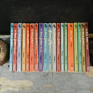 May include: A collection of vintage paperback books from the "Black Stallion" series by Walter Farley. The spines are colorful, with titles like "The Black Stallion Returns" and "Man o' War". The books are arranged on a wooden surface.