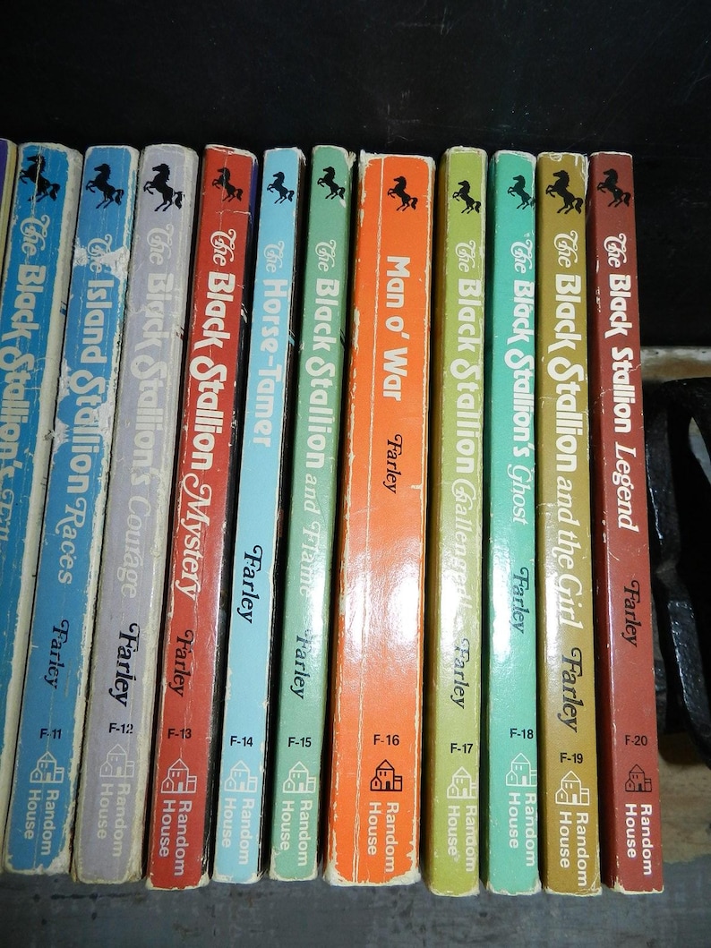 May include: A collection of vintage "Black Stallion" books by Walter Farley. The spines are in various colors, including blue, red, orange, and green, with black horse silhouettes. Titles include "Man o' War" and "The Black Stallion Legend."