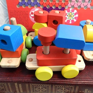 May include: A colorful wooden toy train with red, blue, yellow, and green blocks. The train has wheels and a wooden track. The blocks can be stacked and arranged in different ways.