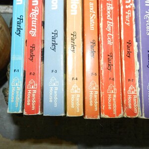 May include: A collection of vintage books with colorful spines. The titles and author's names are visible, including "Farley" and "Random House." The books are in various colors, including blue, red, orange, and purple. The spines are slightly worn, suggesting age.