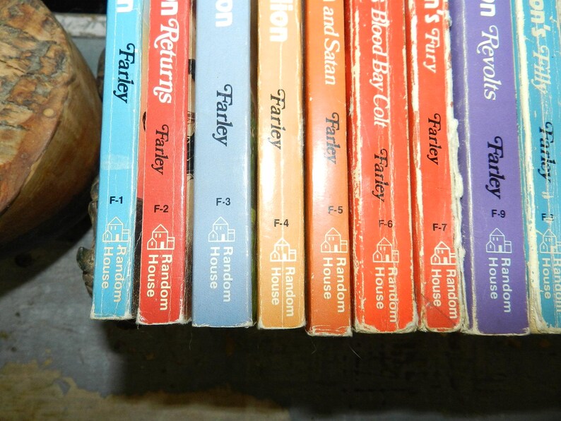 May include: A collection of vintage books with colorful spines. The titles and author's names are visible, including "Farley" and "Random House." The books are in various colors, including blue, red, orange, and purple. The spines are slightly worn, suggesting age.