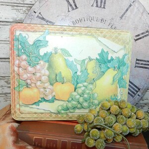 Puede incluir: Un letrero de metal de estilo vintage con una imagen pintada de peras, uvas y manzanas. El letrero tiene un aspecto desgastado y rústico y presenta un fondo marrón claro con hojas y vides verdes.