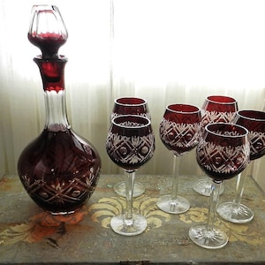 Puede incluir: Un juego de seis copas de vino tinto rubí y una decantador a juego con un tapón de vidrio transparente. Las copas y la decantador tienen un diseño de vidrio tallado.