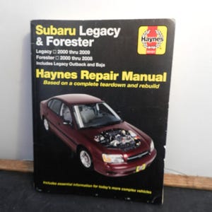 May include: A Haynes Repair Manual for Subaru Legacy & Forester, covering models from 2000 to 2009. The cover features a maroon car with its hood open, set against a black background. The manual includes information for Legacy Outback and Baja.