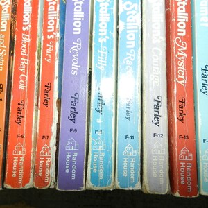 May include: A collection of vintage Farley books, featuring titles like "Stallion and Flame" and "Stallion's Mystery." The spines display various colors, with the author's name and publisher's logo visible. The books are arranged in a row.