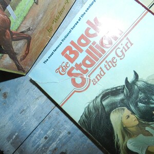 May include: Vintage book cover featuring a black horse and a girl, with the title "The Black Stallion and the Girl." The cover has a light blue background with red and white text. The image also shows a brown horse.
