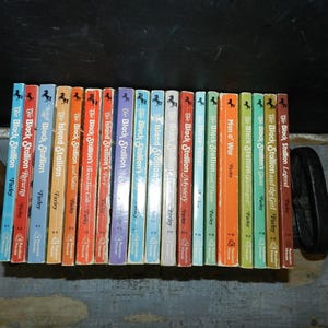 May include: A collection of vintage children's books, featuring titles from the "Black Stallion" and "Island Stallion" series by Walter Farley. The books have colorful spines, including blue, orange, and green, and are arranged in a row.