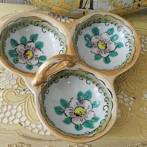 May include: A three-sectioned ceramic serving dish with a handle. Each section features a hand-painted floral design with pink, green, and yellow accents.