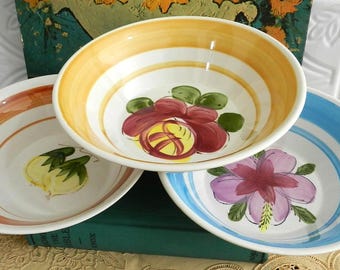 May include: Three ceramic bowls with hand-painted floral designs. One bowl has a yellow and white striped rim with a red and yellow flower. Another has a blue and white striped rim with a purple flower. The third bowl has an orange and white striped rim with a yellow vegetable.
