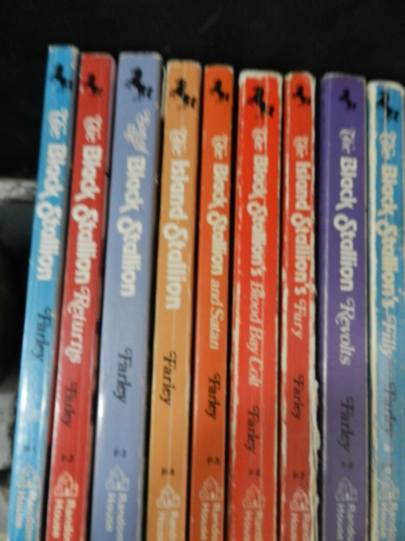 May include: A collection of vintage children's books featuring the "Black Stallion" series by Walter Farley. The spines are in various colors, including blue, red, orange, and purple, with titles and author names visible.