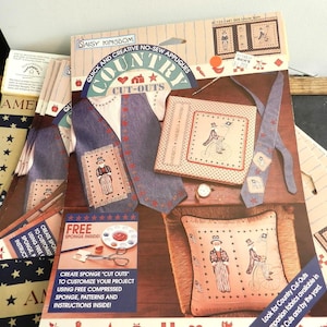 Puede incluir: Un conjunto de recortes de aplicaciones sin coser de temática campestre. El conjunto incluye un chaleco, una corbata, una almohada y un libro pequeño. Los recortes están hechos de tela y tienen un esquema de color rojo, blanco y azul. El conjunto también incluye una esponja gratuita e instrucciones. El texto en el embalaje dice "Aplicaciones sin coser rápidas y creativas Recortes de campo".