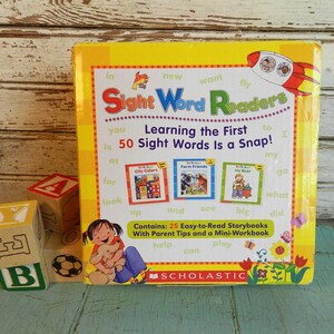 May include: A yellow Scholastic Sight Word Readers box set featuring the text Learning the First 50 Sight Words Is a Snap! and Contains: 25 Easy-to-Read Storybooks With Parent Tips and a Mini-Workbook, accompanied by three wooden alphabet blocks.
