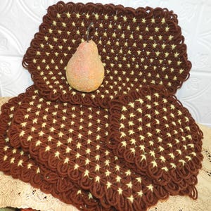 May include: Brown and cream-colored crocheted placemats with a starburst pattern. A decorative pear sits atop the placemats. The placemats have a scalloped edge. The placemats are made of yarn.